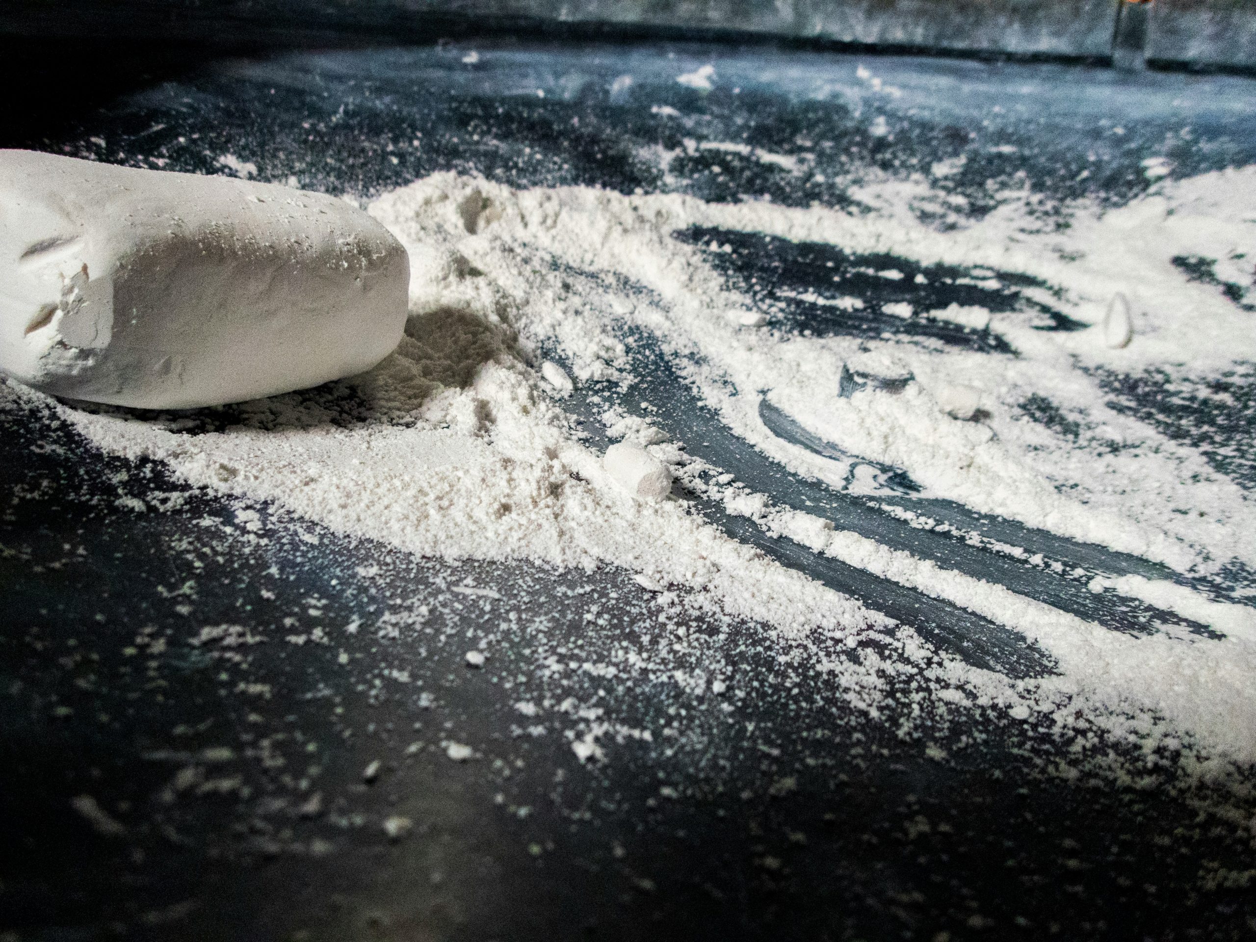 Close-up of white creatine powder and scoop on dark surface, used by strongmen and athletes for muscle boost.