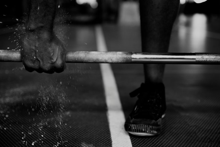 Close-up of a muscular hand gripping a heavy barbell for strength training.