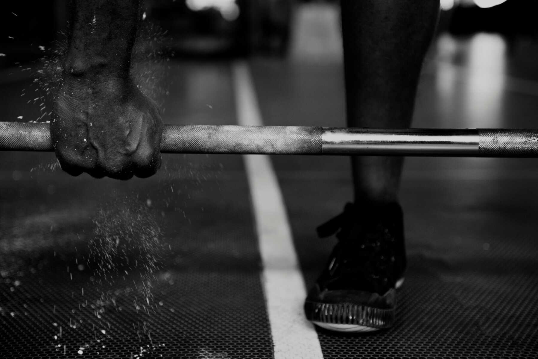 Close-up of a muscular hand gripping a heavy barbell for strength training.