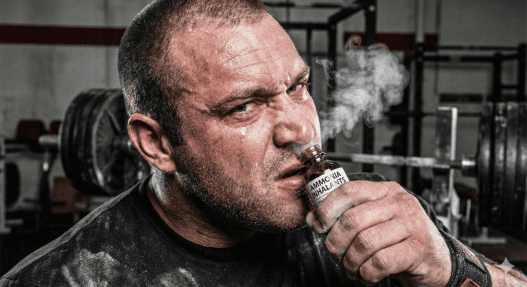 Close-up of an intense strongman lifting athlete with sweat, inhaling ammonia inhalants for focus.