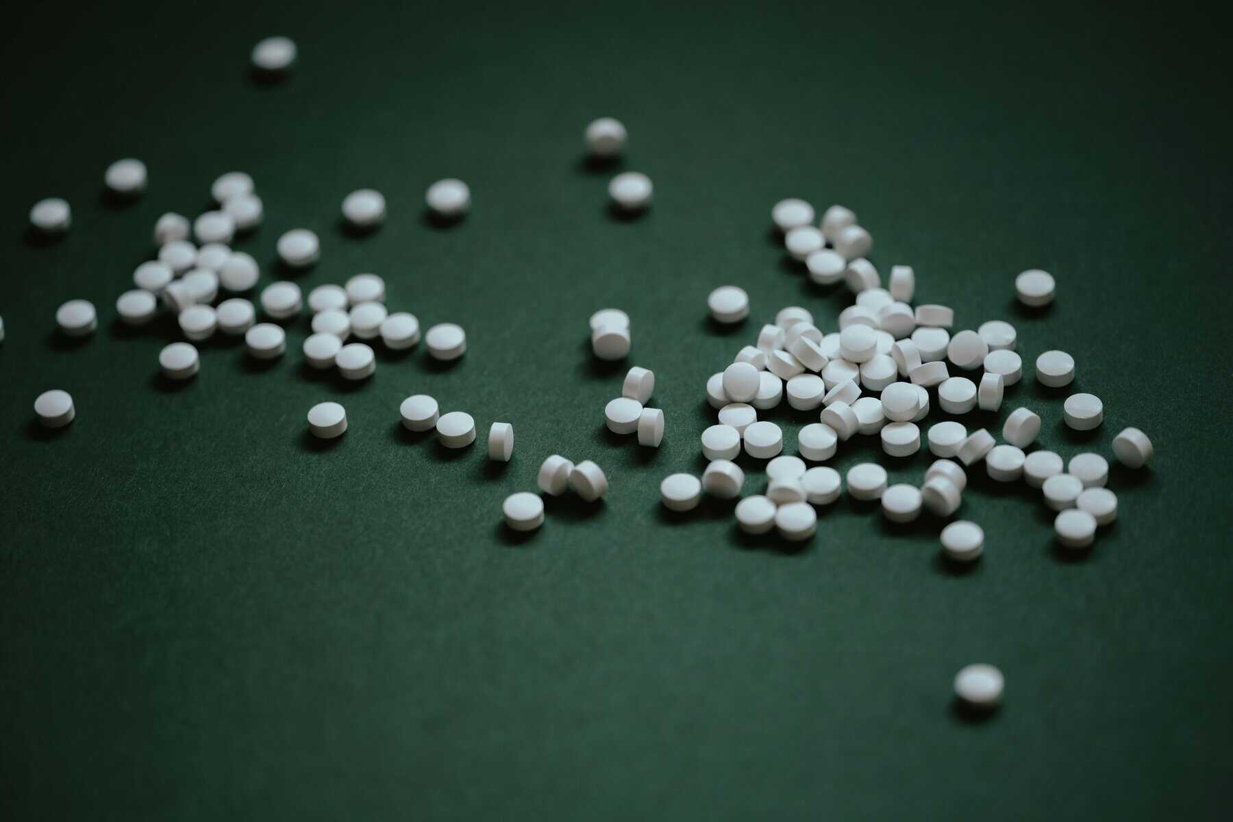 White pills spilled on green table top.